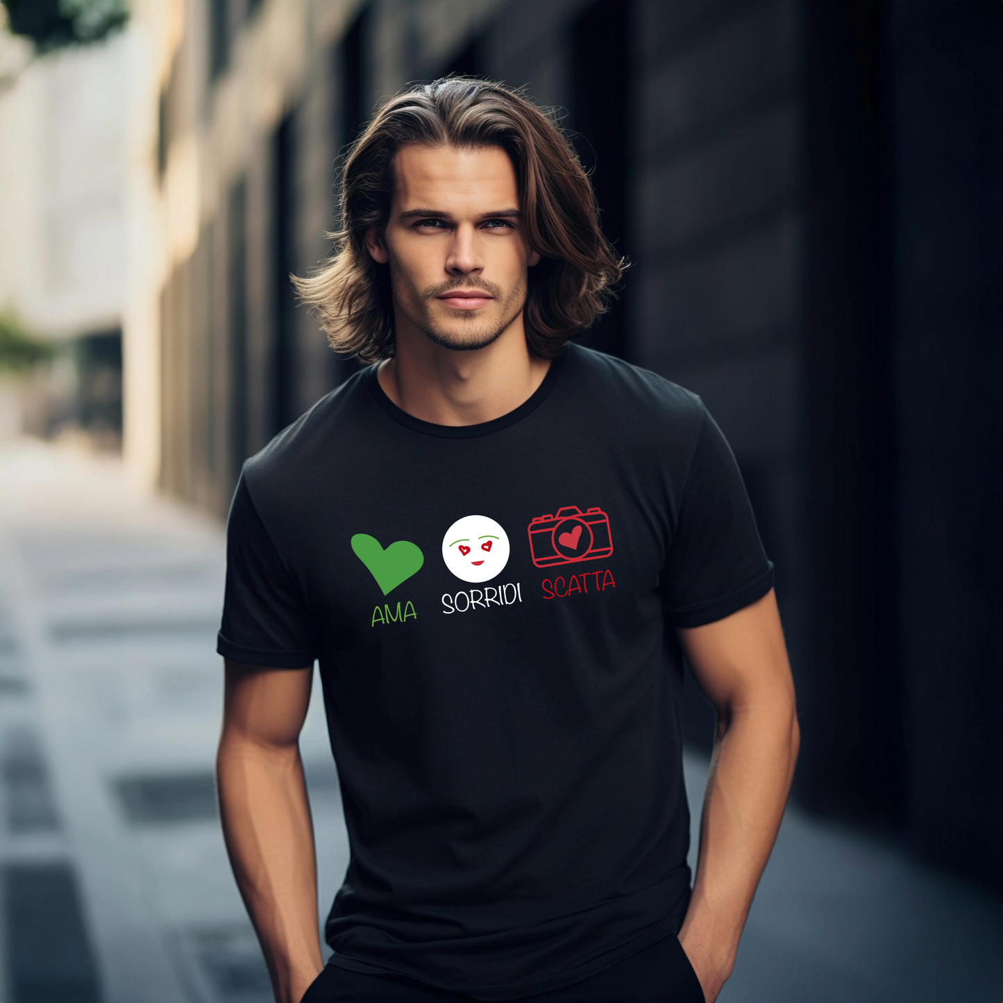 Modello che indossa una t-shirt nera con il design "Ama, Sorridi, Scatta". La grafica presenta un cuore verde, un volto sorridente e una macchina fotografica rossa, ispirata ai colori della bandiera italiana, su uno sfondo urbano