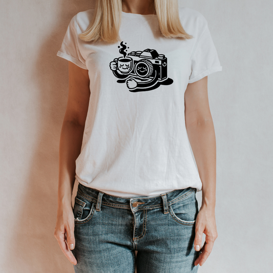 (T-shirt indossata da donna):
Modella indossa una t-shirt bianca con il design “Coffee & Clicks - Il Relax del Fotografo”, raffigurante una macchina fotografica con braccia che tiene una tazza di caffè fumante. Outfit casual con jeans.