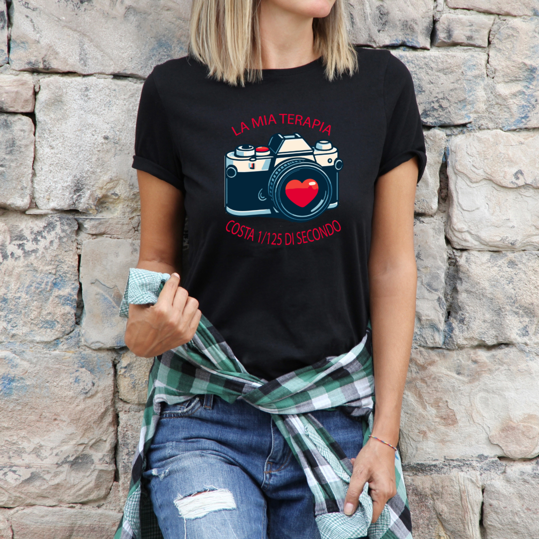 T-shirt nera indossata
"T-shirt nera 'La Mia Terapia' con grafica di macchina fotografica vintage e cuore rosso, indossata da una donna con camicia di flanella e jeans, su sfondo in pietra