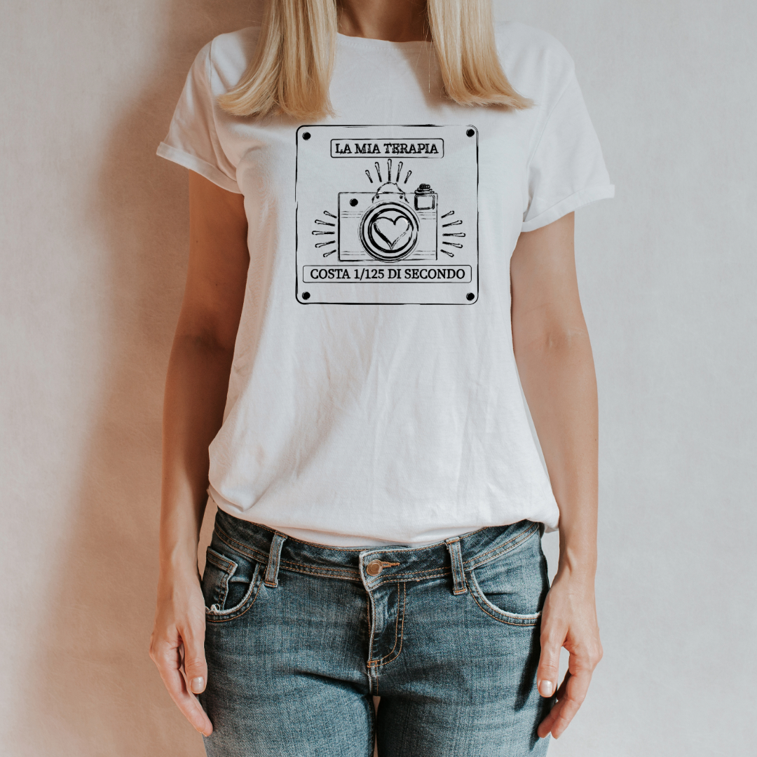 "T-shirt bianca con design fotografico, indossata da una donna con jeans. Stampa con fotocamera e frase motivazionale sulla fotografia."