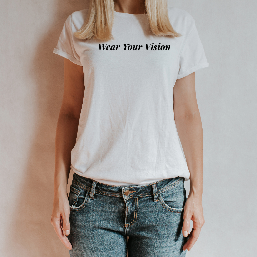 "T-shirt bianca con scritta 'Wear Your Vision' in nero, indossata da una donna con jeans, su sfondo neutro."