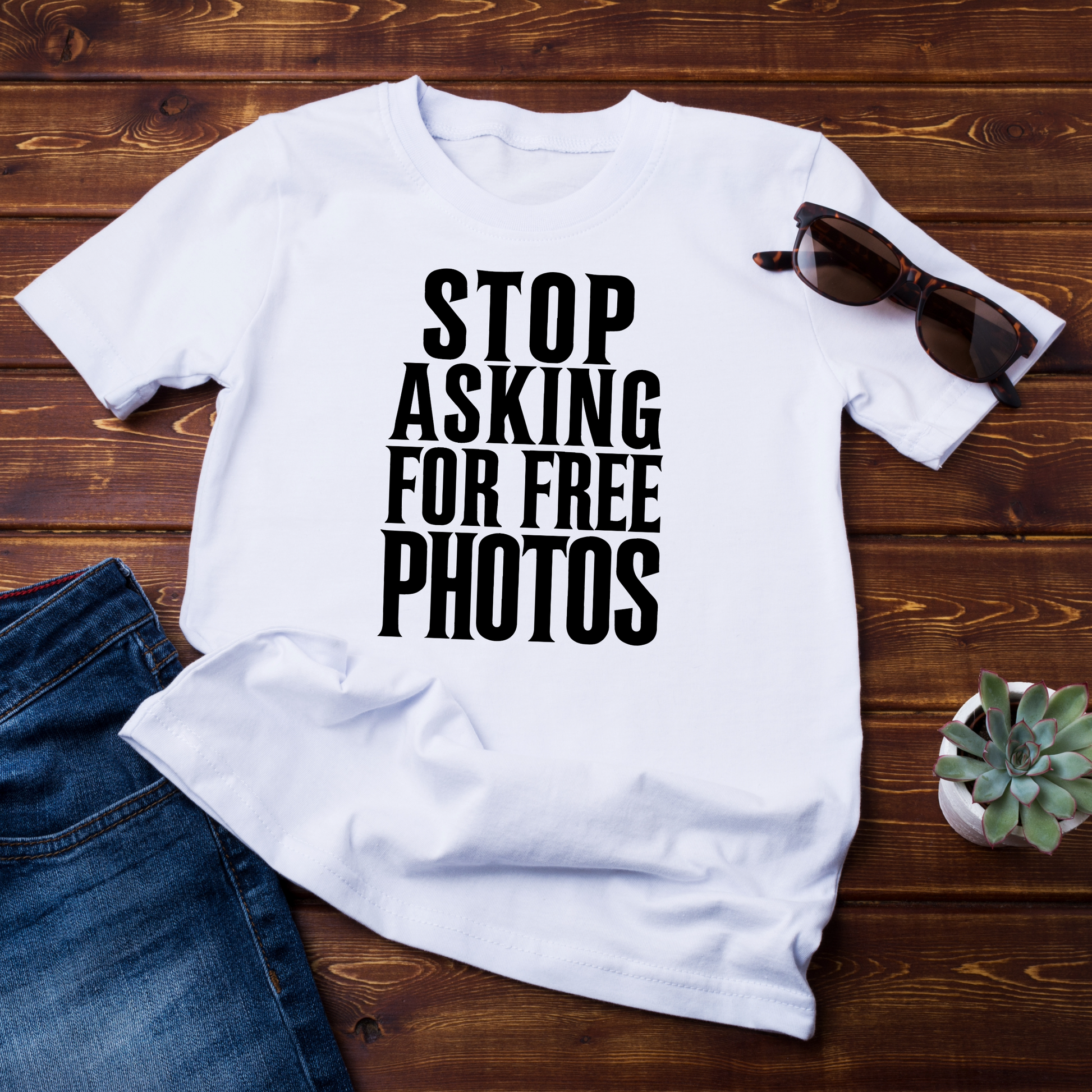 (T-shirt bianca su fondo di legno con occhiali da sole e jeans accanto):
"T-shirt bianca 'Stop Asking for Free Photos' abbinata a occhiali da sole e jeans, un outfit perfetto per i creativi del mondo della fotografia."