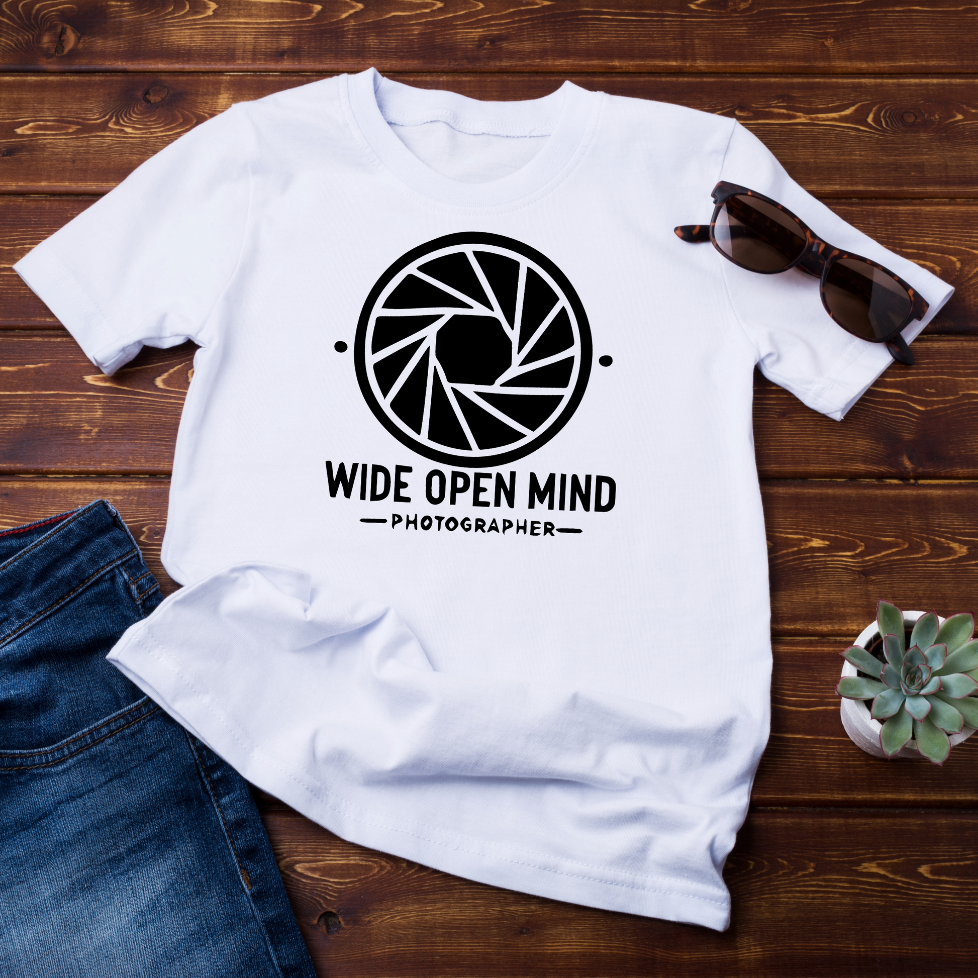 T-shirt bianca "Wide Open Mind" disposta su una tavola rustica con accessori casual, ideale per gli amanti della fotografia.